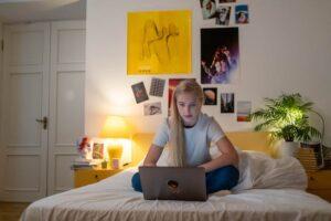 photo of a teen girl sitting on her bad looking at her laptop