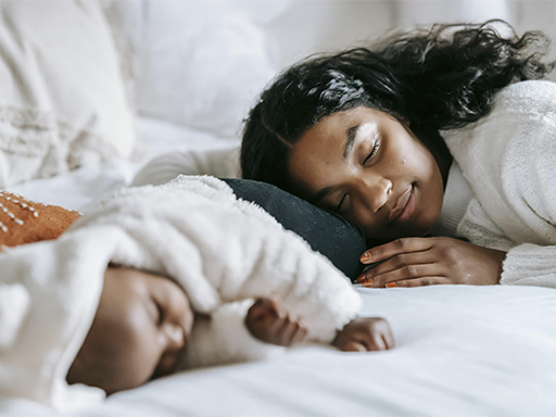 New mom sleeping beside her baby, representing how you can find support for prenatal and postpartum challenges.