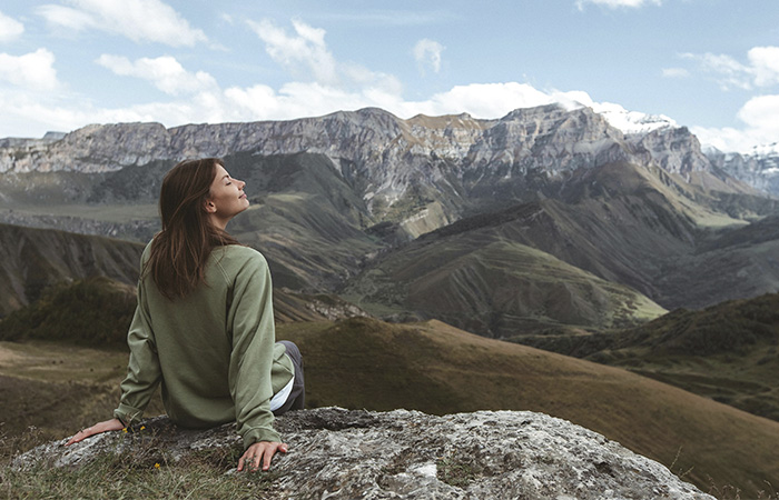 Woman sitting at the top of a mountain looking peaceful, represents the transformation as a therapist from mountain-maker to mountain guide.