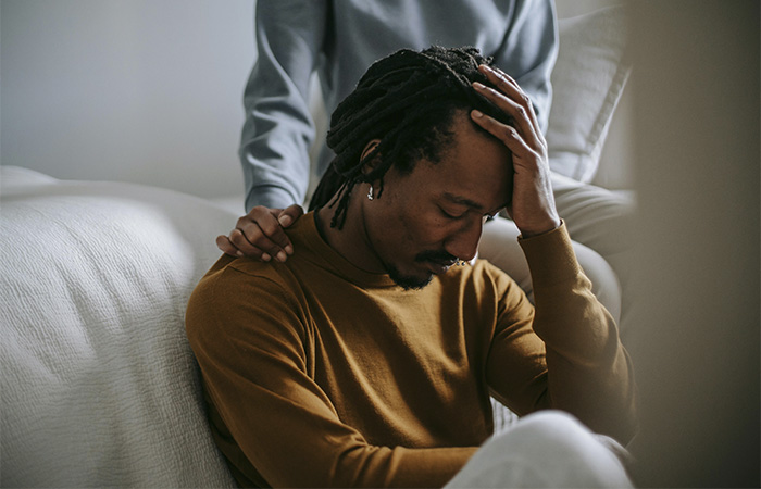 Man holding his head with his hand, looking distressed, while being supported by someone, represents the barriers men face to express emotions due to the masculinity culture.