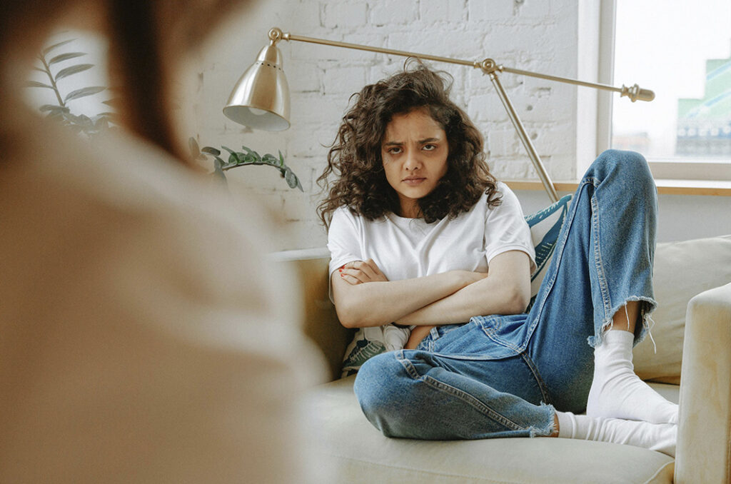Upset teen sitting in the coach across their parent, represents how parents can learn the signs of depression in teens.