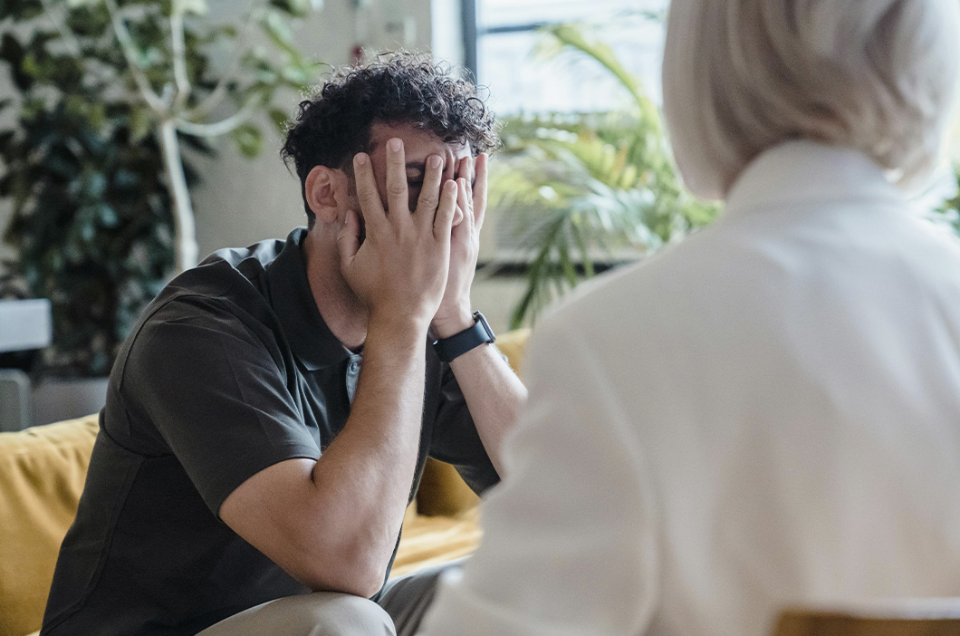 Man hiding his head in his hands while talking to a woman, represents how many men today are struggling with a masculinity crisis.