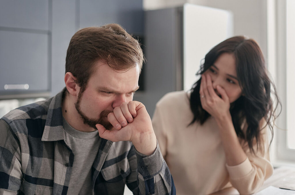 Man looking upset while his partner seems to be hiding a smile, represents the signs of a toxic relationship.
